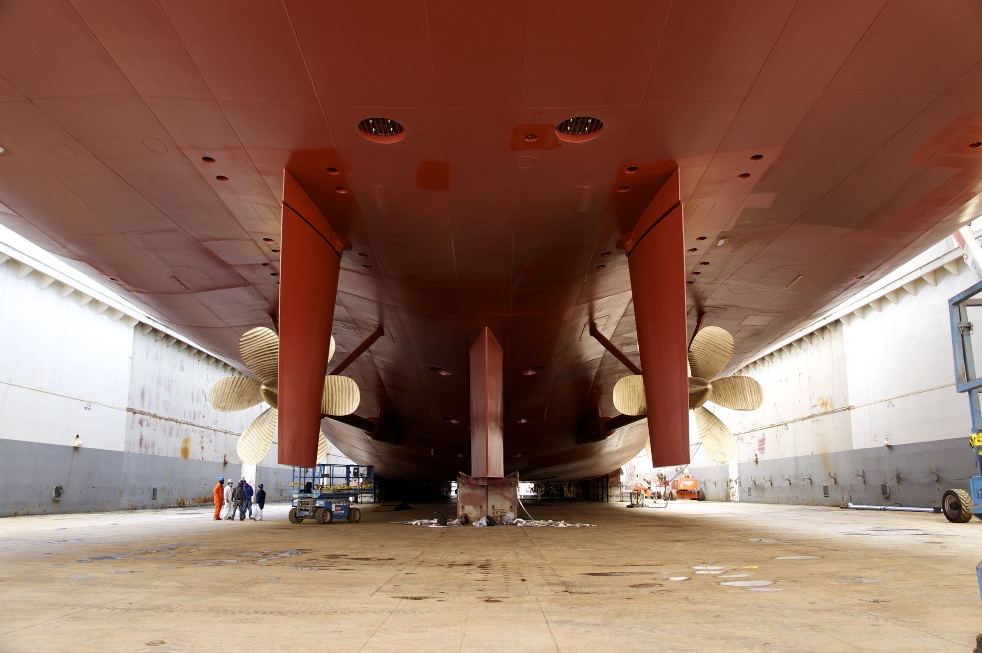 Shipyard workers inspecting a ship's hull and propellers in dry dock